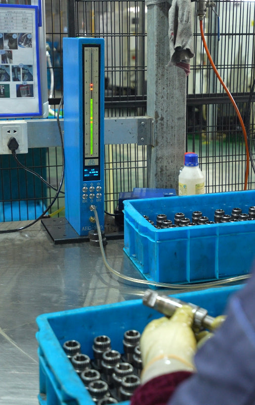 Operator handling a metal component beside an air gauge and blue parts bins.