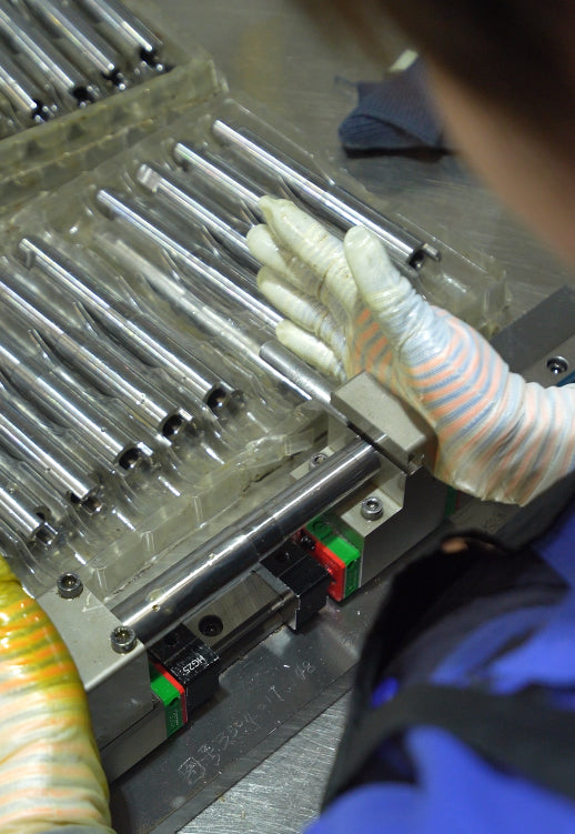 Gloved operator checking a shaft component with a go/no-go gauge.
