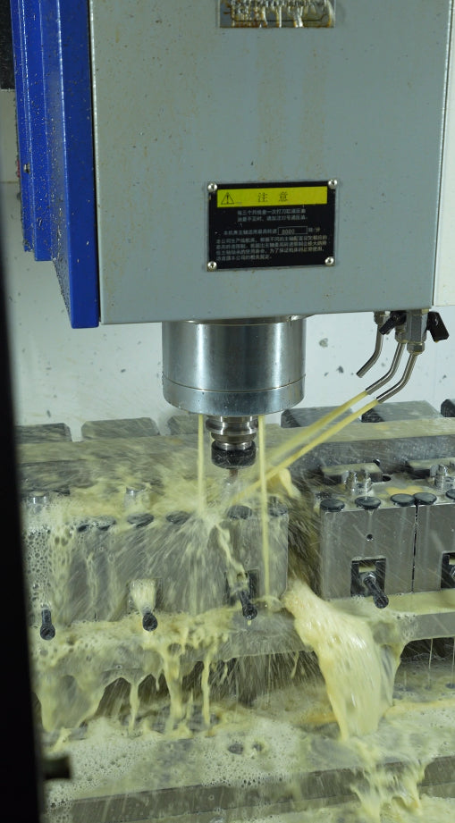 Vertical milling spindle above clamped workpieces with coolant flowing across the fixture.
