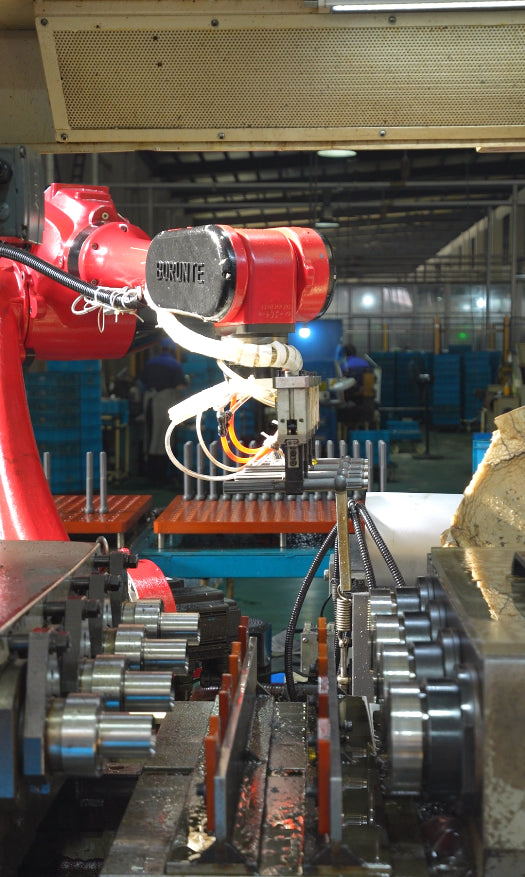 Robot gripper above fixtures and shaft workpieces at a gun-drilling station.